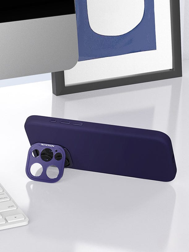 A MagSafe-Compatible iPhone 16 Pro Max Case with Silicone Grip & Aluminum Camera Kickstand rests on a white desk in a horizontal position. The detachable aluminum camera kickstand is shown separately in front of it. A computer monitor and framed artwork are in the background, highlighting the case's eco-friendly liquid silicone that supports MagSafe wireless charging.