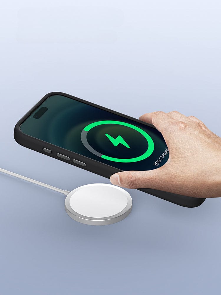 A hand places an iPhone 16 Pro Max, encased in a MagSafe-Compatible iPhone 16 Pro Max Case with Silicone Grip & Aluminum Camera Kickstand, onto a MagSafe wireless charger. A green circle and lightning bolt icon on the phone screen indicate that charging is in progress.