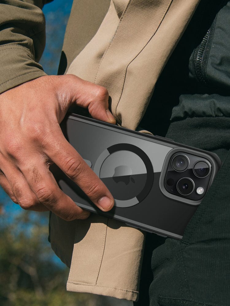 A person in a two-toned jacket is holding an iPhone 16 Pro Max Magnetic Ring Stand Case with full body shockproof protection and a camera control button, against their side.