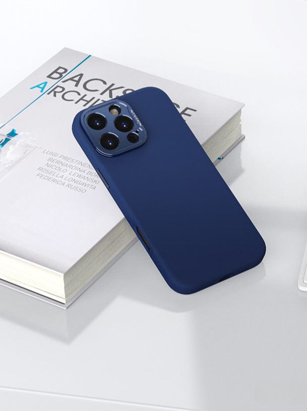 A smartphone with a blue, eco-friendly MagSafe-Compatible iPhone 16 Pro Max Case featuring a silicone grip and aluminum camera kickstand is placed on top of a book titled "Backstage Architecture" on a white surface.