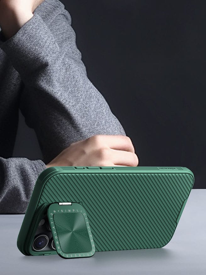 Shockproof Slim Fit iPhone 16 Pro Max Case with MagSafe, Dual-Layer Protection & Camera Cover in green, featuring a foldable stand propping up a phone in landscape orientation on a table, with a person in a gray sweater resting their arm nearby.