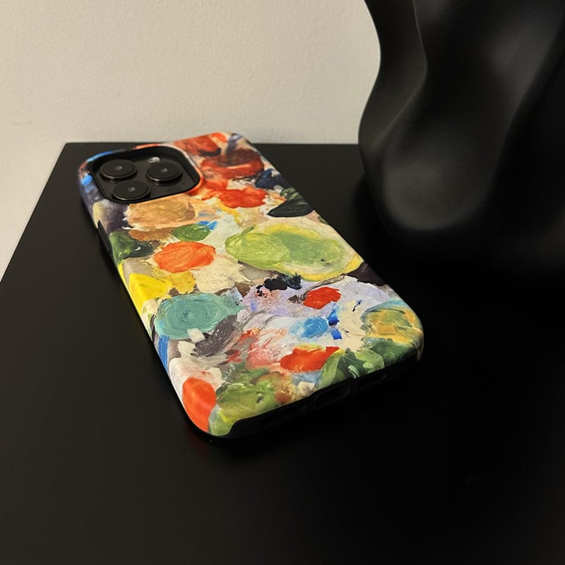 An Abstract Paint Palette iPhone 16 Pro Max Case - Artistic and Protective is placed on a black surface, with a small abstract black sculpture partially visible in the background.