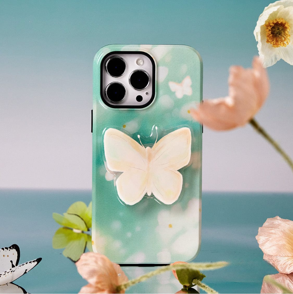 The Butterfly Blossom MagSafe iPhone 16 Pro Max Case features a large white butterfly in the center, surrounded by smaller butterflies and pink and white flowers, creating an elegant floral design. The all-inclusive protective cover also includes a stand for added convenience.