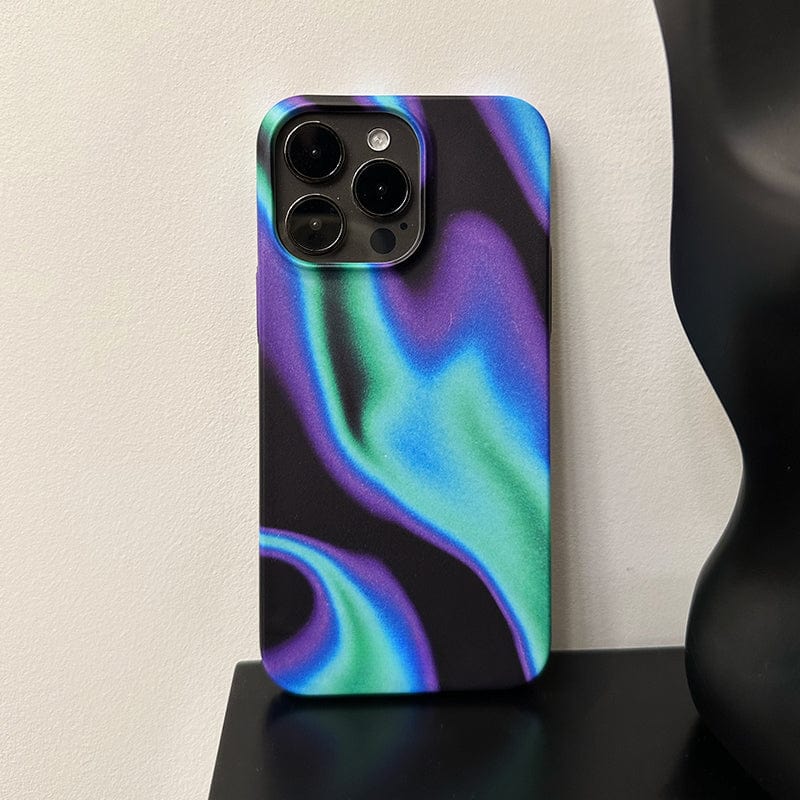 An iPhone 16 Pro Max with an Iridescent Waves case, featuring a sleek and futuristic design in shades of blue, green, and purple, is leaning against a white wall. The camera lenses are prominently visible, and a part of a black object is beside it.