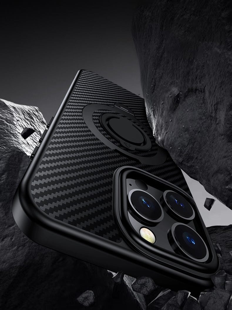 Close-up of an iPhone 16 Pro Max encased in a military-grade, black carbon fiber-finished cover with triple camera lenses and a 360° rotating kickstand on its back, nestled among jagged rocks.