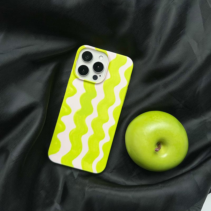 A smartphone with a Vibrant Wavy Line iPhone 16 Pro Max Case - Bold Lime Green & Cream Design, Ultra-Slim, Protective Cover rests on a black fabric background. Beside it, there is a green apple.