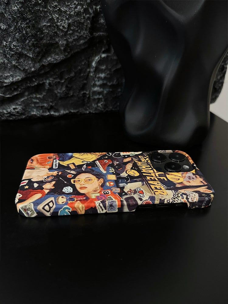 A smartphone with a Vibrant Collage iPhone 16 Pro Max case, featuring pop art, street style, and retro design elements, is placed on a black surface. The background includes a black, textured object that appears to be a decorative piece.