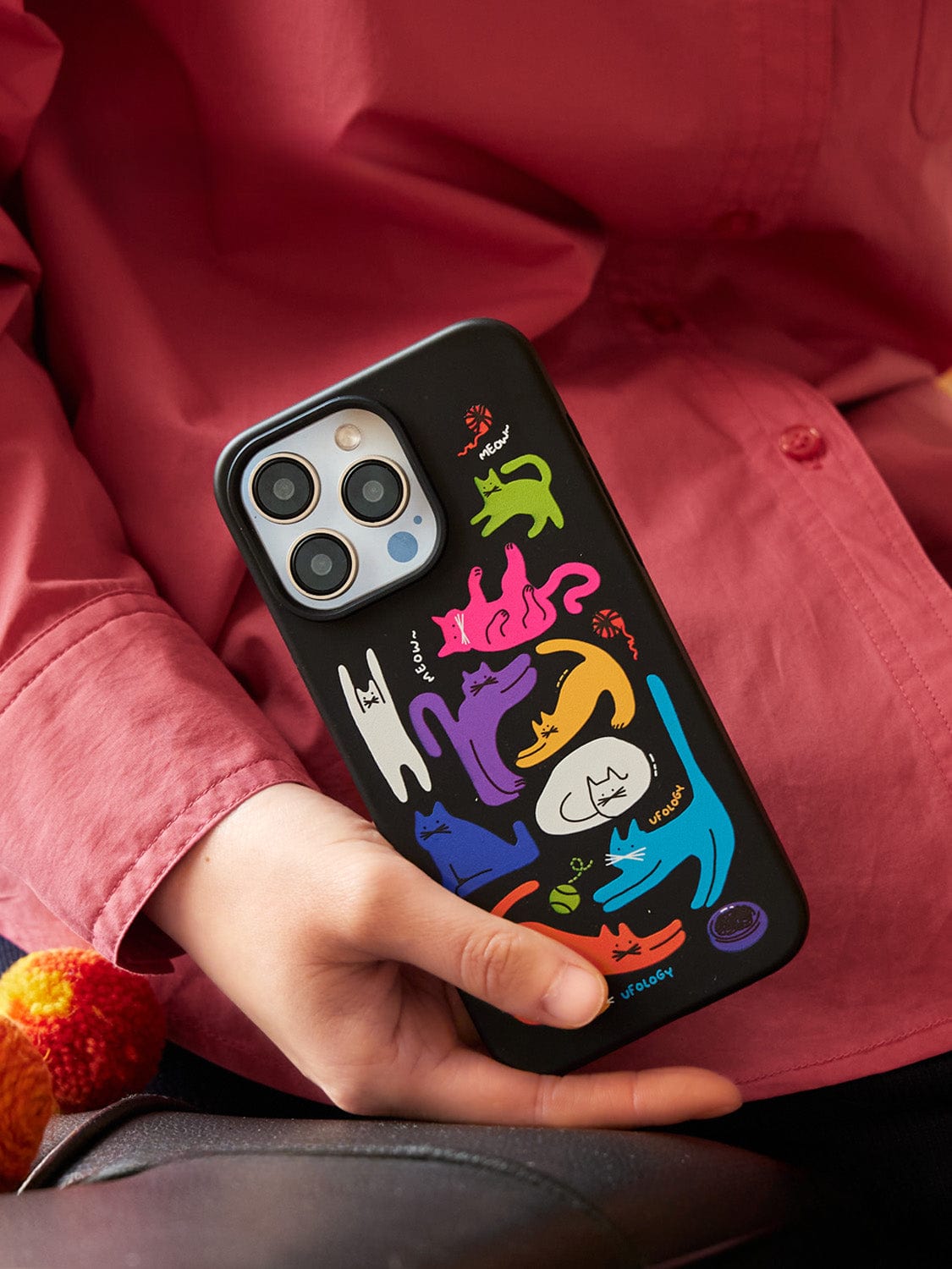 Hand holding a smartphone with a Colorful Cats MagSafe iPhone 16 Pro Max Case featuring a vibrant cat-themed design and stand, contrasted against a pink shirt background. The colorful and vivid design beautifully complements the sleek look of the all-inclusive protective cover.