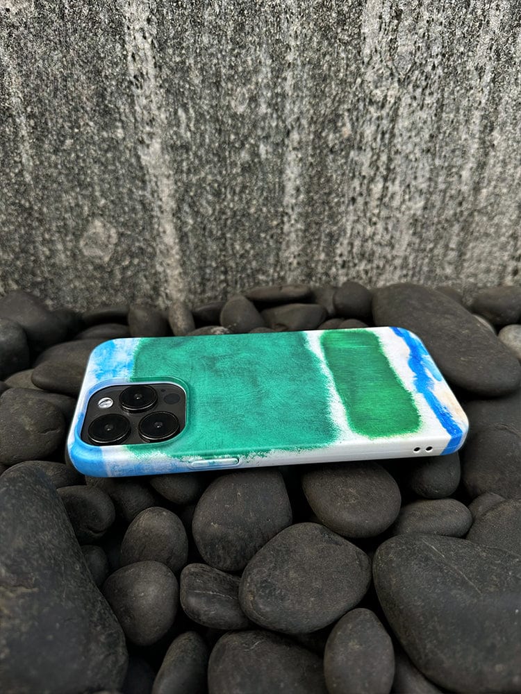 Resting on smooth black stones, a smartphone dons an Abstract Color Block iPhone 16 Pro Max Case, showcasing a modern art-inspired, minimalist design with vibrant green and blue hues. With its camera lenses prominently visible, the colorful back cover faces up against a textured gray wall in the background.