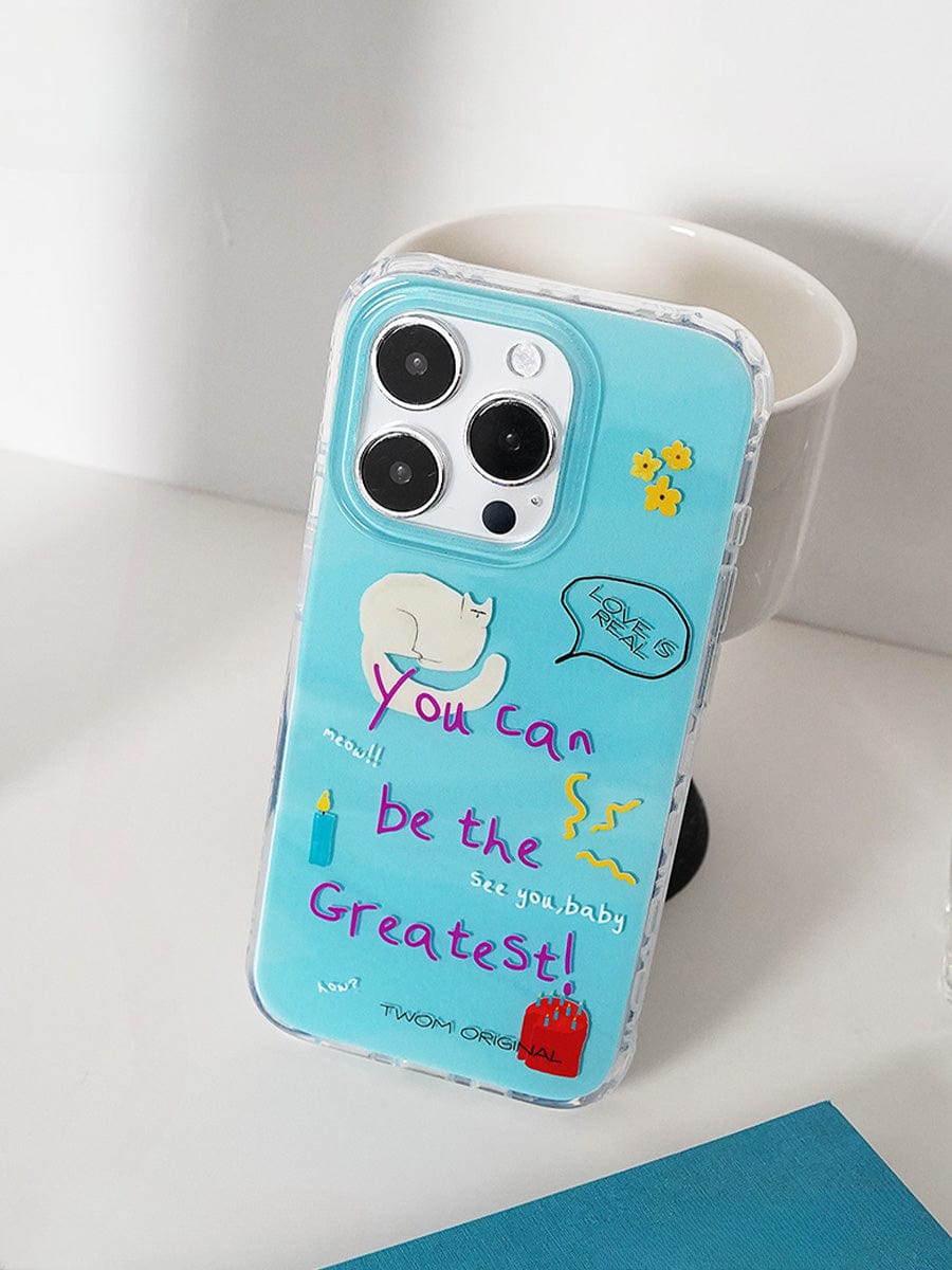 A smartphone with a "You Can Be the Greatest iPhone 16 Pro Max Case | Fun Motivational Design | Playful All-Inclusive Protective Cover," showcasing a cat illustration and motivational text, "You can be the greatest!" rests on a white surface next to a white cup.