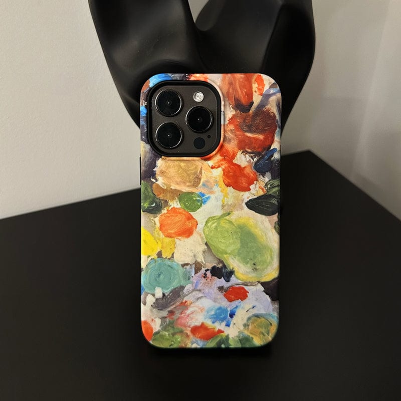 An iPhone 16 Pro Max with an Abstract Paint Palette case, both artistic and protective, is placed on a black surface. The background features part of a black sculpture.