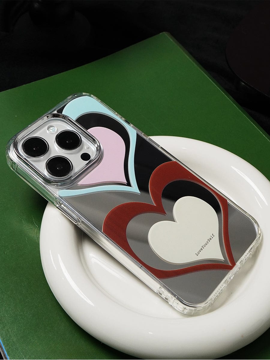 A Retro Heart Layers iPhone 16 Pro Max Case with a vibrant "Love Yourself" design rests on a white plate placed on a green surface.