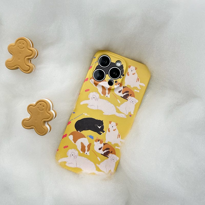 The Playful Pups iPhone 16 Pro Max Case - Cute Dog Pattern Design with Full Protection, in a vibrant yellow shade adorned with delightful dog illustrations, rests on a fluffy white surface. Adjacent to it are two gingerbread-shaped cookies, and the phone case's camera lenses are prominently visible at the top.