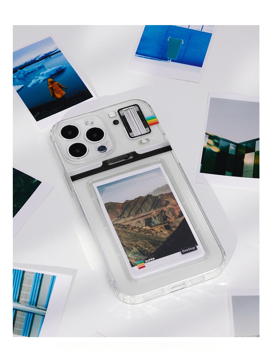 A Polaroid Frame MagSafe iPhone 16 Pro Max case, designed with a customizable photo holder and faux instant camera look, features a small landscape picture inside. It rests on a white surface surrounded by various printed photos.