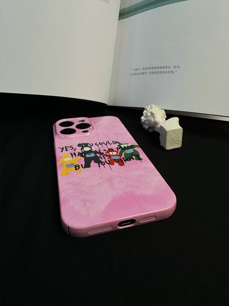 A Playful Critique iPhone 16 Pro Max Case - Bold Pink Design with Unique Artistic Statement featuring the text "YES, YOU COULD HAVE AN EPIC BIRTHDAY!" rests on a dark surface. Behind it, there's an open book with text and a small white decorative item resembling a miniature statue.