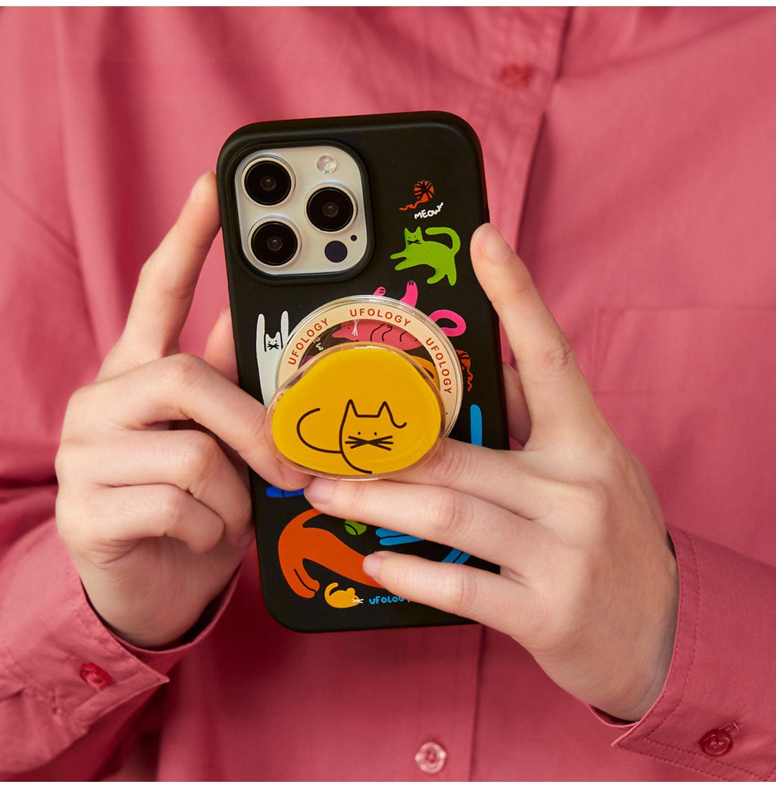 Person wearing a pink shirt holding the Colorful Cats MagSafe iPhone 16 Pro Max Case adorned with colorful cat stickers and a yellow pop socket featuring a cat drawing.