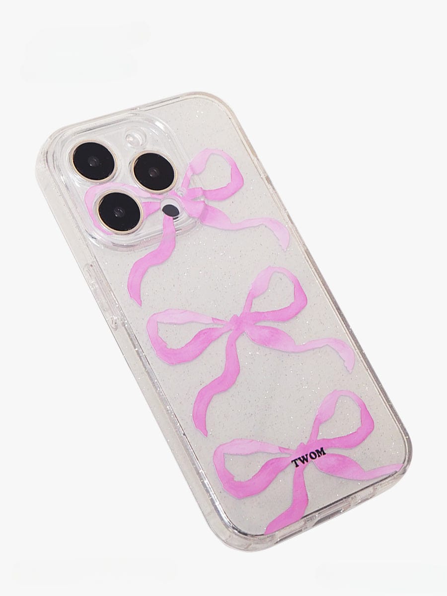 The "Pink Ribbon Bow Transparent iPhone 16 Pro Max Case | Sparkling Clear Design | Elegant All-Inclusive Protective Cover" features three pink ribbon drawings on the back. This clear case is fitted on an iPhone 16 Pro Max with a triple-lens camera, and the brand name "TWOM" is printed towards the bottom. The backdrop is a plain white background.