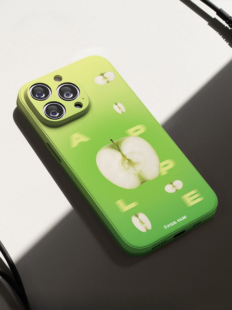 The Green Apple Fresh iPhone 16 Pro Max Case with its vibrant gradient green and yellow back cover lies on a white surface. The cover features the word "APPLE" in white letters, each letter containing a small apple image. The camera lenses are visible at the top left corner of the device.