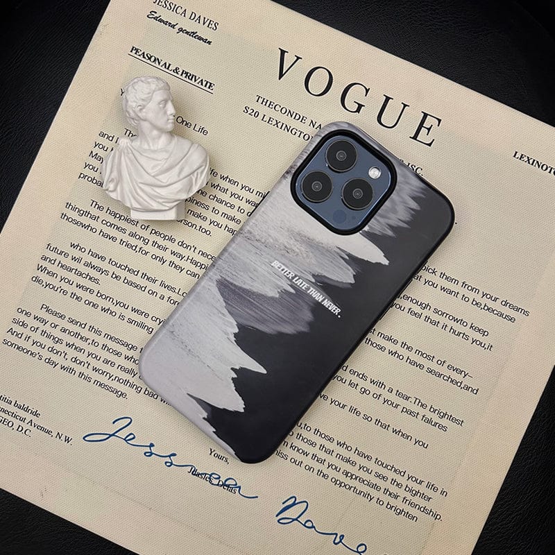 An iPhone 16 Pro Max encased in a Monochrome Waves case, featuring a minimalist black and gray abstract design with the quote "Better Late Than Never," is placed on top of a printed document resembling a magazine page with the title "VOGUE." A small white bust sculpture is positioned on the top left corner of the page.