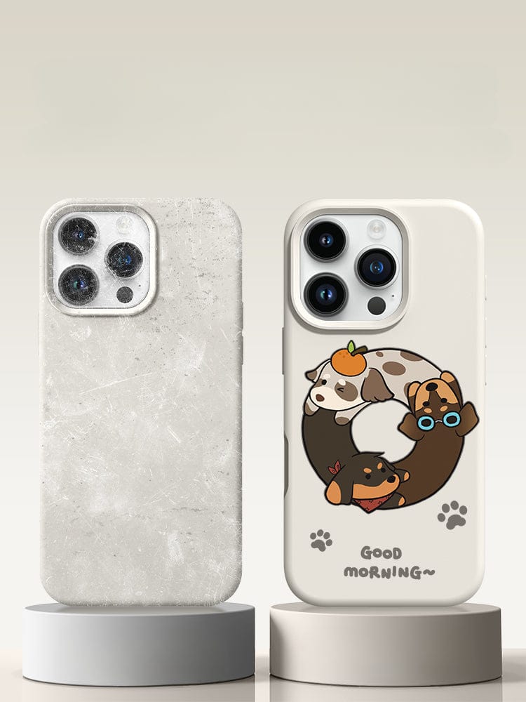 Two smartphone cases are displayed on stands. The left case has a marble texture, while the right case is an iPhone 16 Pro Max Case - Good Morning Cartoon Dog Silicone Protective Cover featuring adorable cartoon dogs with the text "Good Morning~", offering triple-layer protection and a washable design that is both shockproof and anti-yellowing.