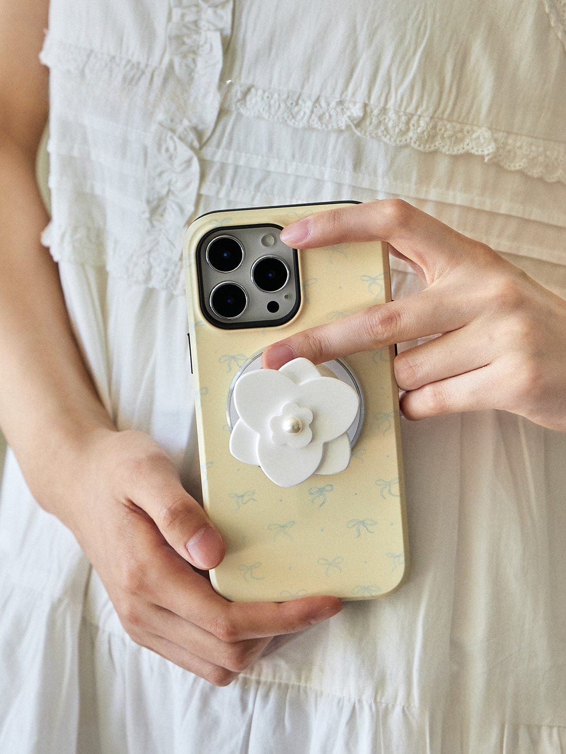 Person in a white dress holding a smartphone with an Elegant Blossom MagSafe iPhone 16 Pro Max case, featuring a chic floral design and integrated pearl flower stand.