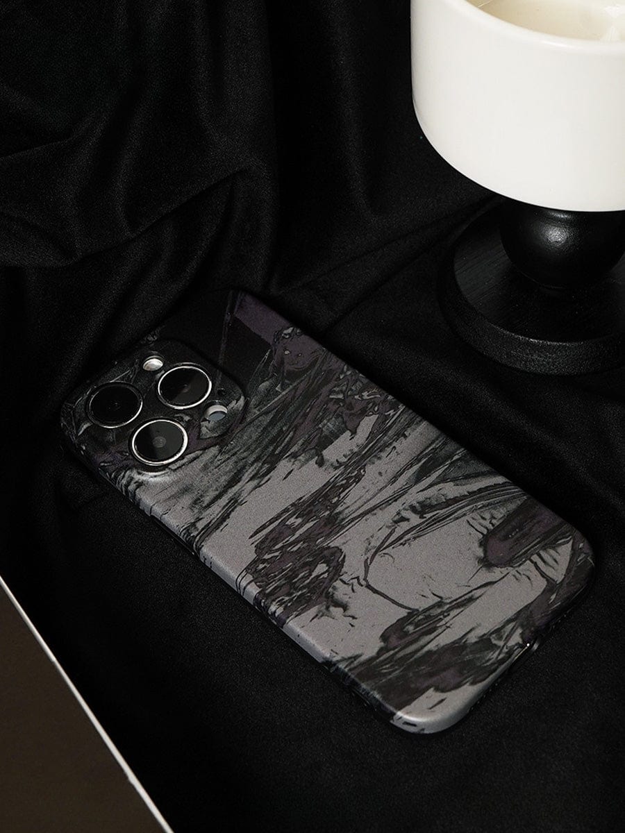 A smartphone with a Monochrome Marble iPhone 16 Pro Max Case featuring an abstract artistic design lies on a black fabric surface next to part of a small, white and black object.