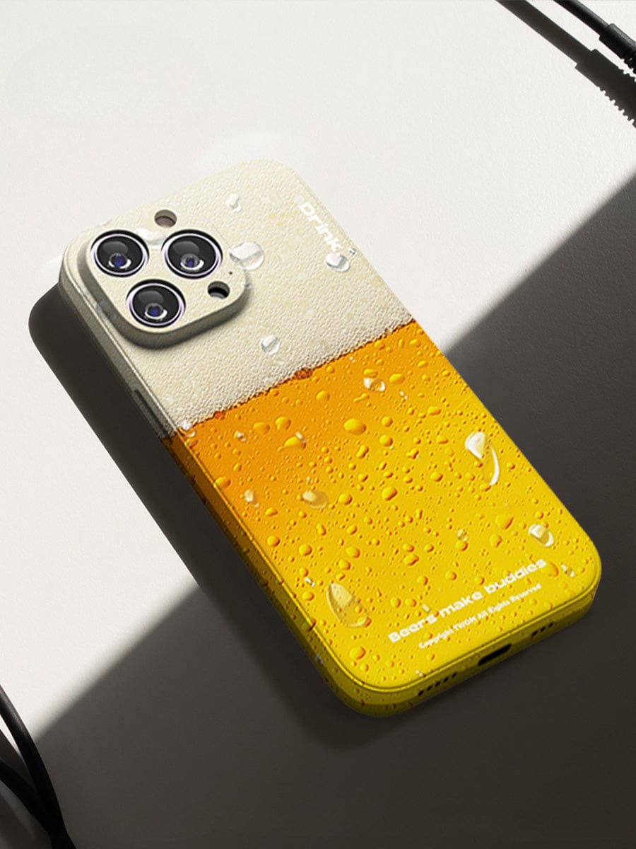 The Beer Buddies iPhone 16 Pro Max Case, featuring a fun beverage design that resembles a glass of beer complete with realistic condensation droplets, lays on a surface with headphones partially visible.