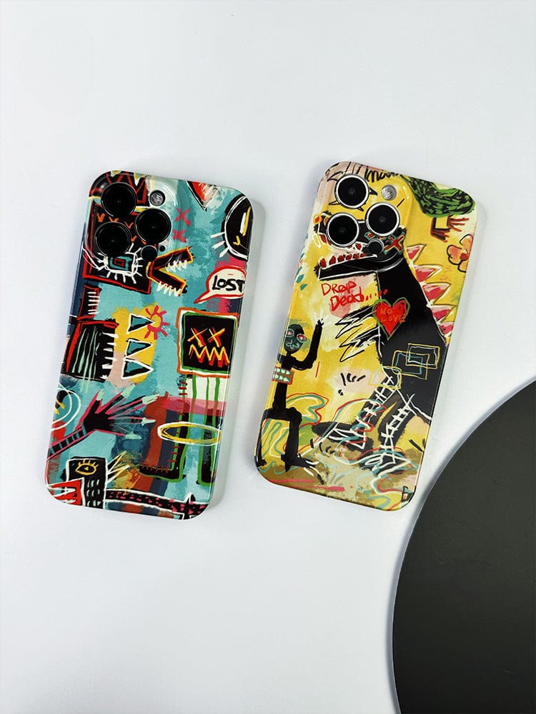 Two smartphones adorned with colorful, abstract, and graffiti-style designs on their back covers are displayed on a white surface. The phone on the left showcases a mix of geometric shapes and vibrant colors, while the phone on the right features a stylized dragon and text artwork—both part of the Urban Graffiti iPhone 16 Pro Max Case Set from the Bold Street Art Collection.