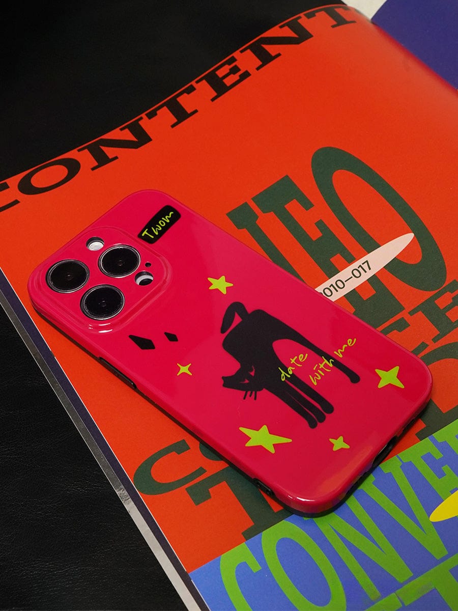 A Dare With Me Black Cat iPhone 16 Pro Max Case with a bold red design, featuring a black cat and yellow stars, is placed on a colorful magazine cover with bold text.