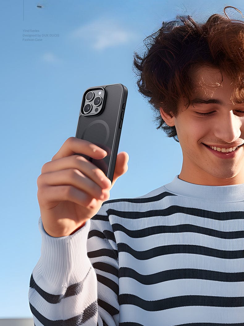 A person wearing a striped shirt holds an iPhone 16 Pro Max Case - Matte Finish, MagSafe Compatible, Anti-Fingerprint, Shockproof PC Backplate in their hand, smiling and looking at the device against a clear blue sky background.