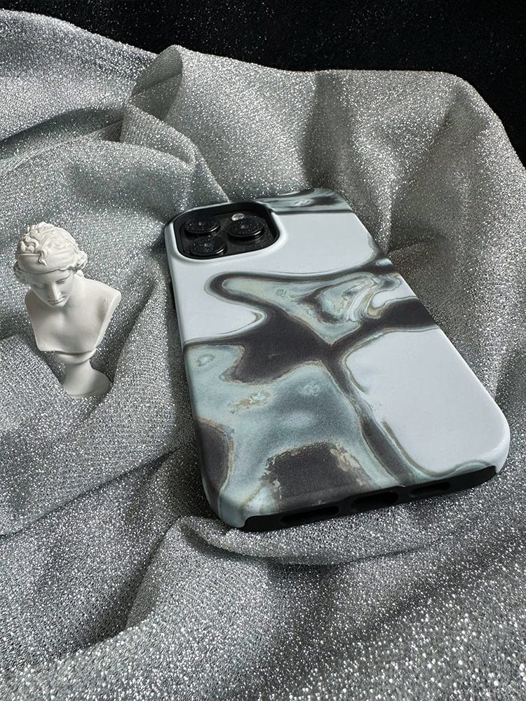 A smartphone encased in the Abstract Metallic Flow iPhone 16 Pro Max Case, featuring a sleek modern art design, is placed on sparkly, silver fabric. Beside it sits a small white bust statue of a person. The overall setting exudes a luxurious feel.