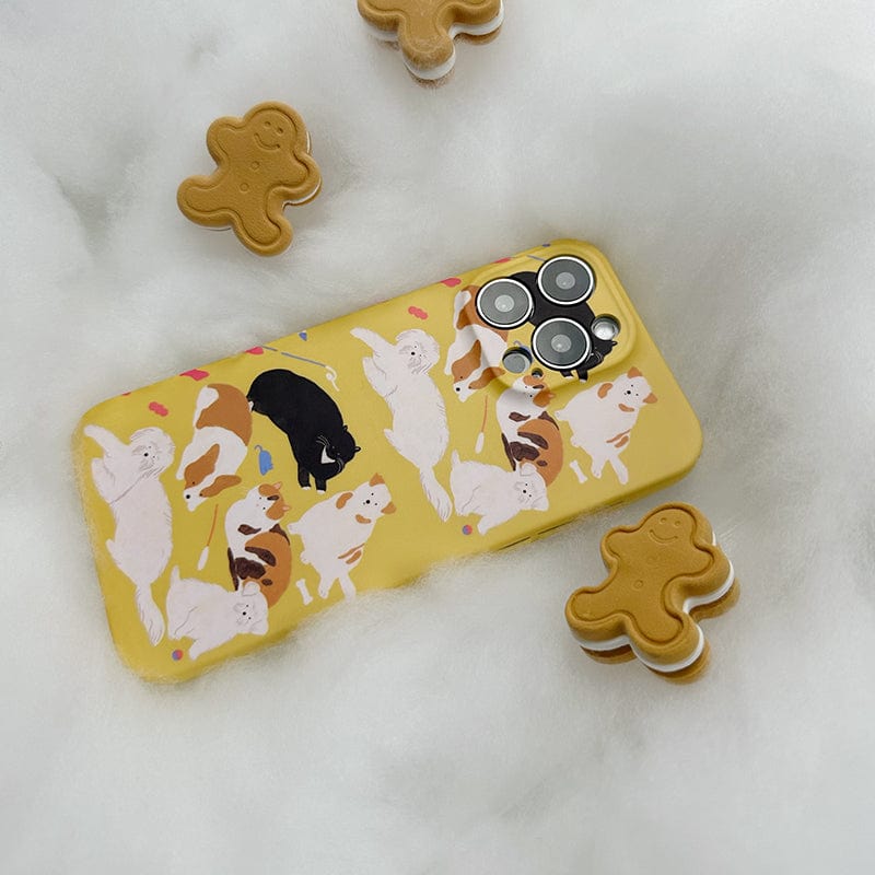 A yellow smartphone with a Playful Pups iPhone 16 Pro Max Case featuring an illustrated cute dog pattern, surrounded by several gingerbread man-shaped cookies. The phone is placed on a soft, white, fluffy surface.