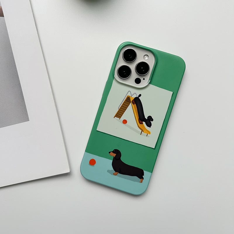 The "Playful Dachshund iPhone 16 Pro Max Case - Cute Green & Blue Design, Ultra-Slim, Durable Protection" features a green cover with a whimsical dachshund design. At the top, a cartoon dachshund is depicted climbing a slide, and the bottom showcases another dachshund near an orange ball against a minimalistic background with clean lines.