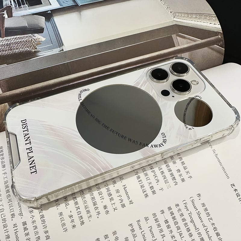 A transparent "Futuristic Distant Planet iPhone 16 Pro Max Case - Sleek and Protective" is placed on an open book. The case features the text "DISTANT PLANET" along with "Take pictures as if the picture was far away." Its design also includes camera lens cutouts and reflective elements.