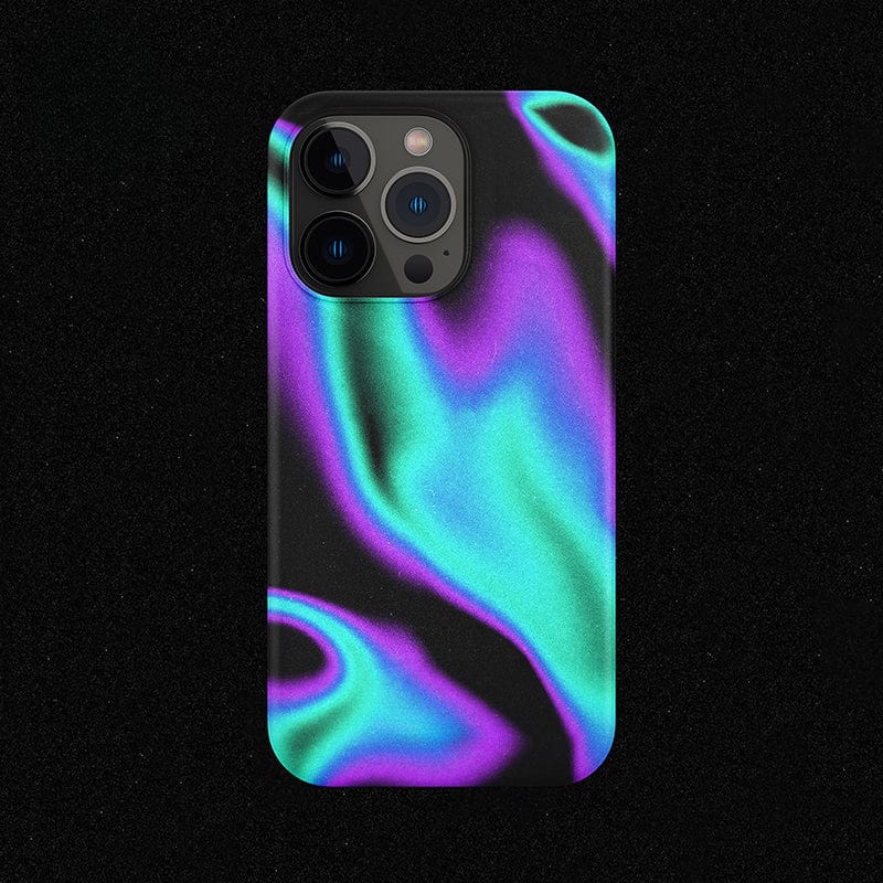 An Iridescent Waves iPhone 16 Pro Max Case lies on a black surface, showcasing a vibrant, swirling pattern in green, purple, and blue hues. The phone's camera lenses are prominently visible at the top left corner of the device.