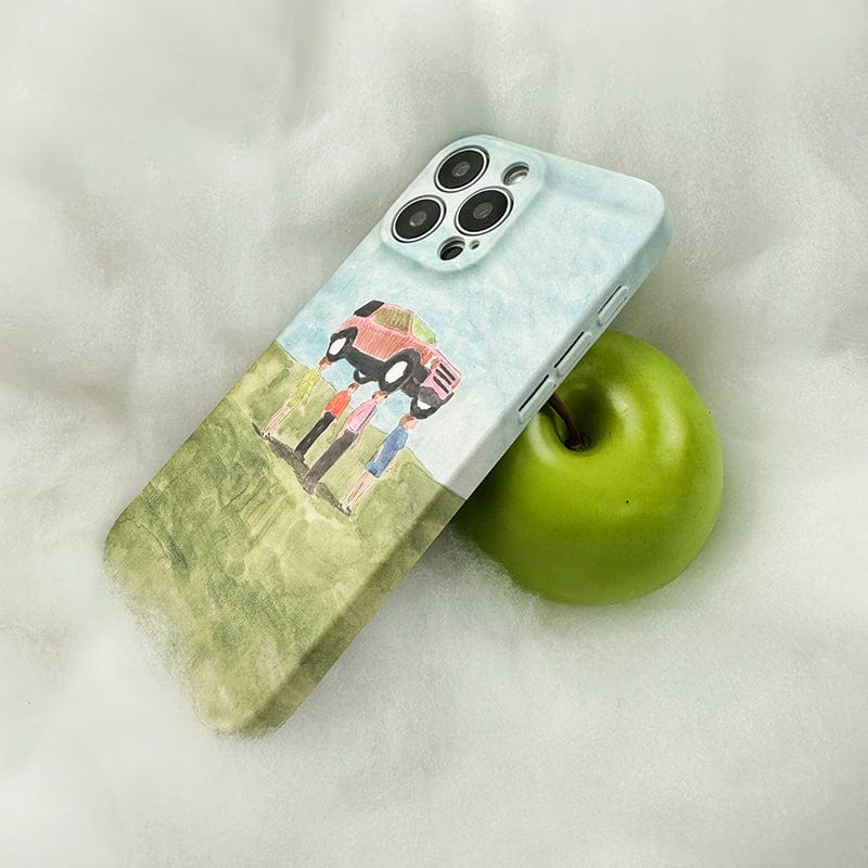 A smartphone encased in the Surreal Car Lift iPhone 16 Pro Max Case, adorned with whimsical watercolor art of a family next to a car, is placed on a soft, white surface. The phone is propped up against a green apple.