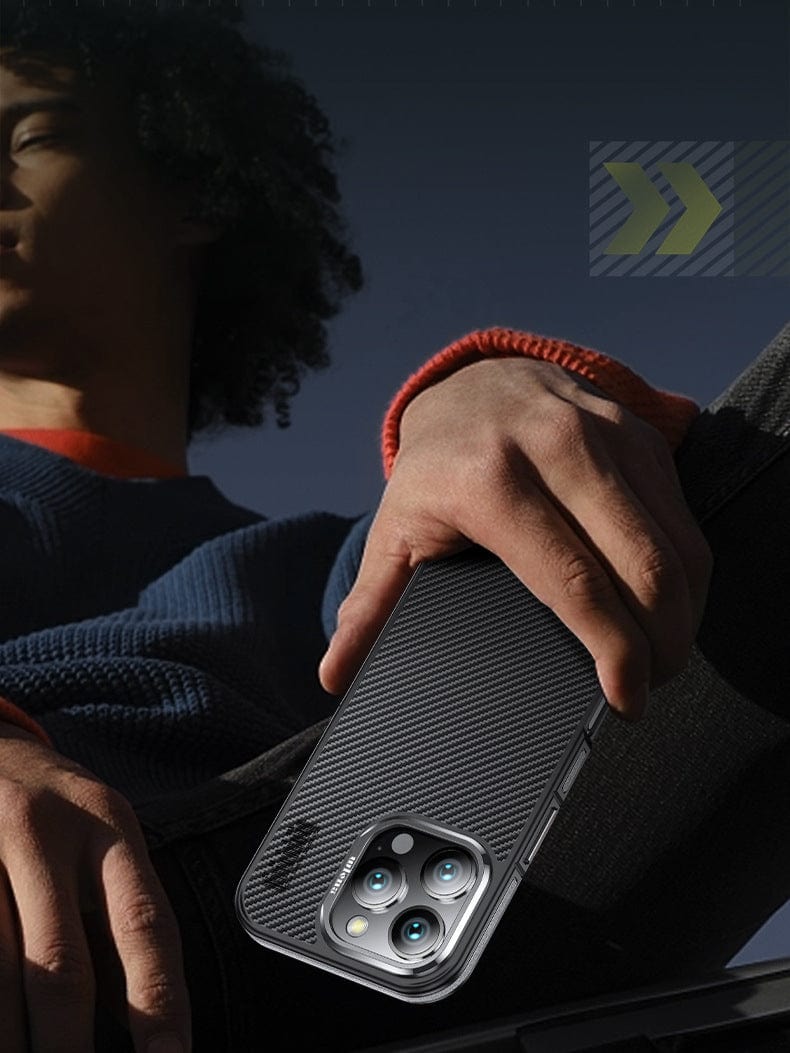 An individual in a blue sweater is outdoors, holding an iPhone 16 Pro Max equipped with the N52 Magnetic MagSafe Case, a shockproof cover made from 600D Aramid Fiber. The phone features triple cameras.