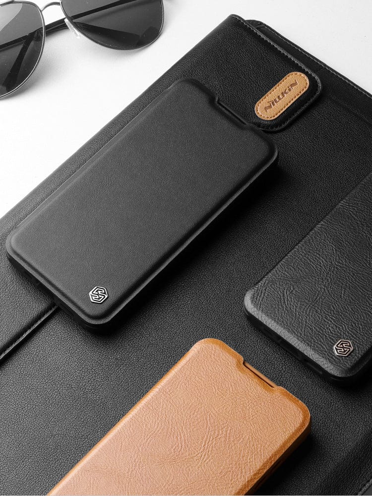 A pair of sunglasses, black and brown phone cases, and an iPhone 16 Pro Max Leather Flip Case with Card Holder featuring full protection, a metal lens cover, and a stand feature are arranged on a white surface.