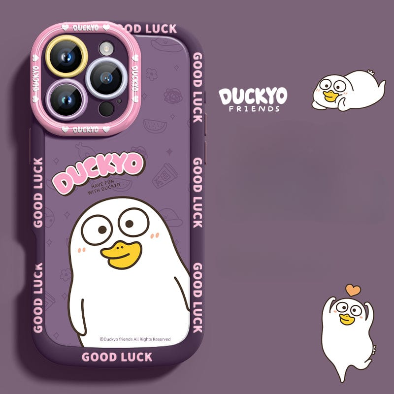 A purple iPhone 16 Pro Max Yellow Duck Cartoon Case made of soft liquid silicone, featuring a cute, yellow cartoon duck character with the text "DUCKYO" and "GOOD LUCK" prominently displayed. The background also includes additional smaller images of the duck, offering shockproof protection while providing a slim-fit, anti-yellowing design for your phone.