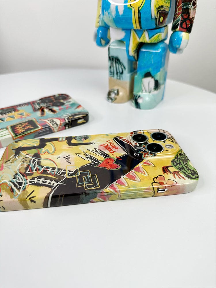 Two smartphones with Urban Graffiti iPhone 16 Pro Max Case Set - Bold Street Art Collection and a customized collectible figurine are displayed on a white surface. The phones and figurine feature vibrant, graffiti-style artwork with various colors and abstract designs.