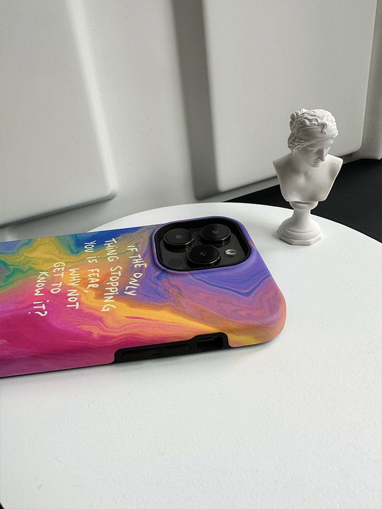 An Inspirational Swirl iPhone 16 Pro Max Case - Colorful Abstract Design with Motivational Quote, featuring text that reads, "The only thing stopping you is fear. What do you want to know?" is lying on a black and white surface. Next to the phone is a small, white bust of a classical figure.