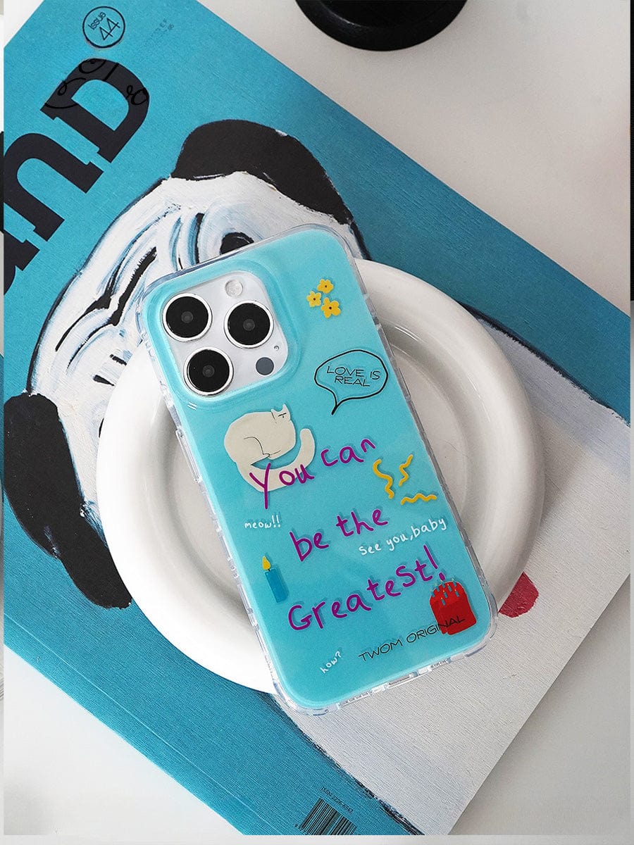 The You Can Be the Greatest iPhone 16 Pro Max Case, adorned with fun motivational designs and playful cartoon graphics, encases a smartphone. The device, in its vibrant blue shell, rests on a circular white dish atop a partially visible magazine with a matching blue cover.