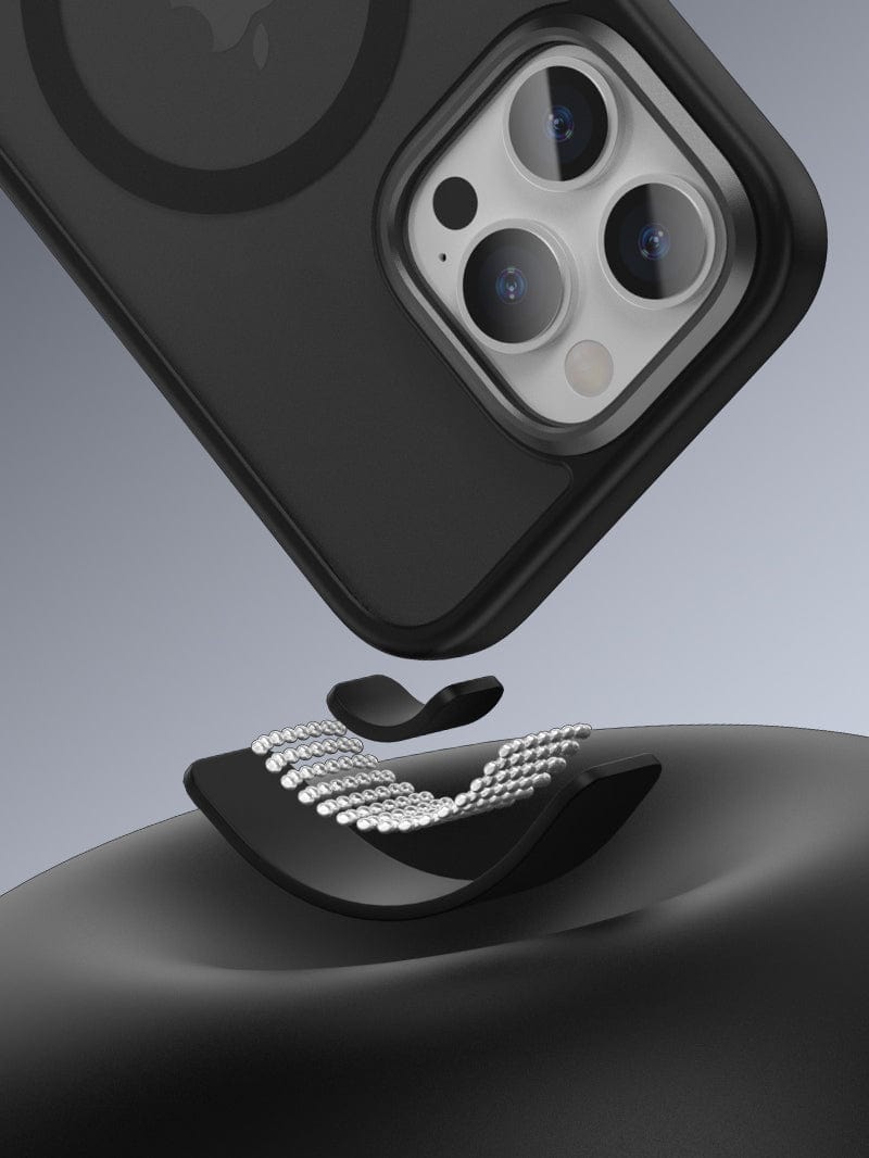 A black iPhone with a Golden Shield iPhone 16 Pro Max MagSafe Case is attached to a MagSafe-compatible magnetic wireless charger, viewed from an angled perspective. The case offers anti-fingerprint and shockproof protection, featuring an aluminum alloy camera frame for added protection and style.