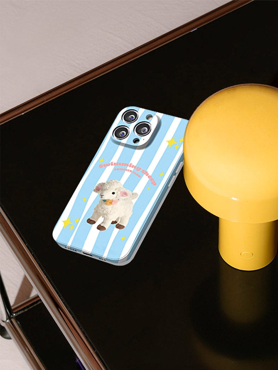 A smartphone with a Swimming Sheep iPhone 16 Pro Max Case, showcasing a cute striped design, lies on a dark surface next to a yellow lamp.