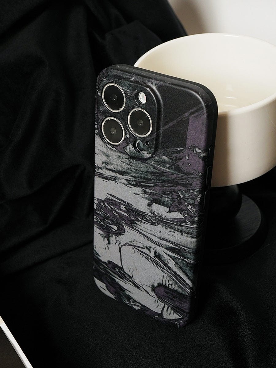 A smartphone with a Monochrome Marble iPhone 16 Pro Max Case, featuring an abstract black and white artistic design, is placed against a black cloth background beside a white cup.