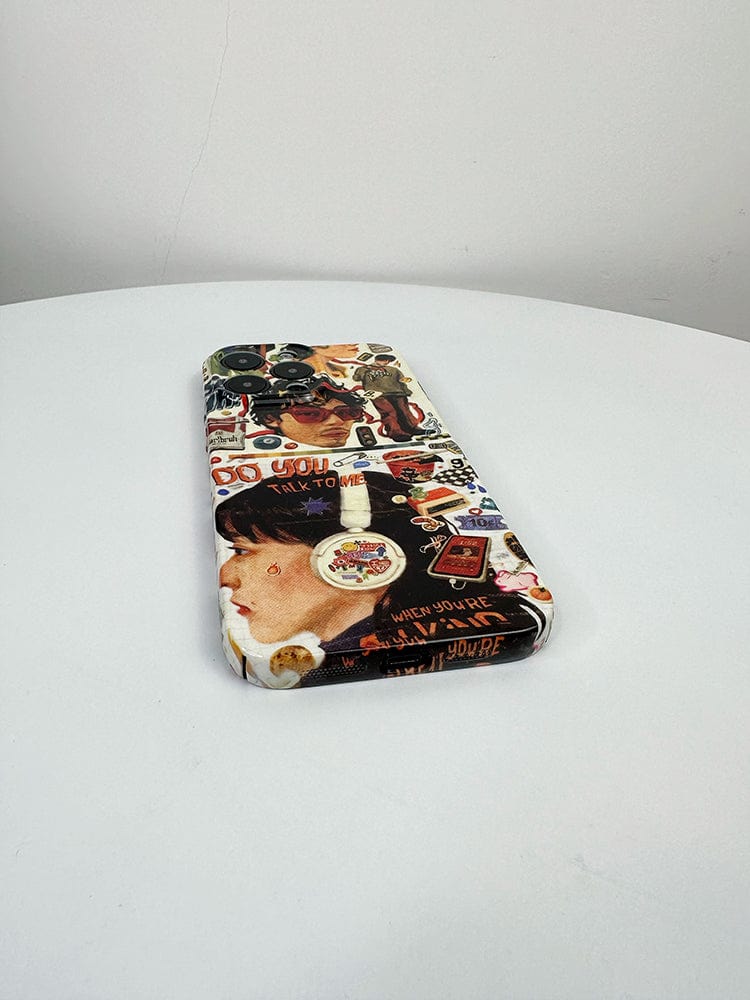 A smartphone adorned with the Retro Collage iPhone 16 Pro Max Case - Artistic and Protective, which showcases a vibrant array of images and text, lies flat on a round, white table. The eclectic design features pictures of faces, objects, and words against a plain and light background.