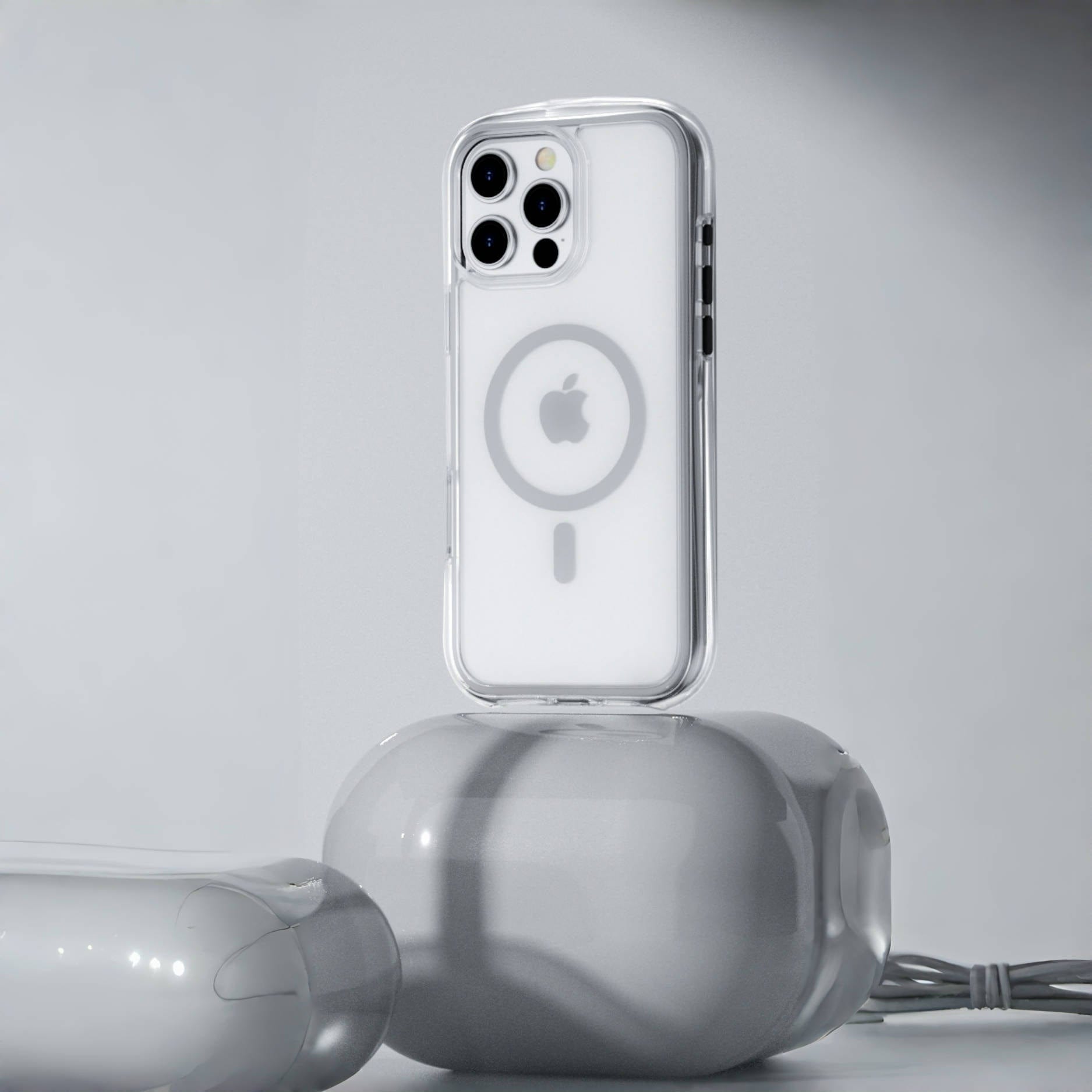 A smartphone with a clear, white Air Cushion MagSafe Case, showcasing a visible Apple logo, stands on a reflective, spherical surface. A coiled cable is seen on the side, emphasizing the iPhone 16 Pro Max’s sleek design and the robust shock absorption features of its 360° Shockproof Clear Protective Cover.