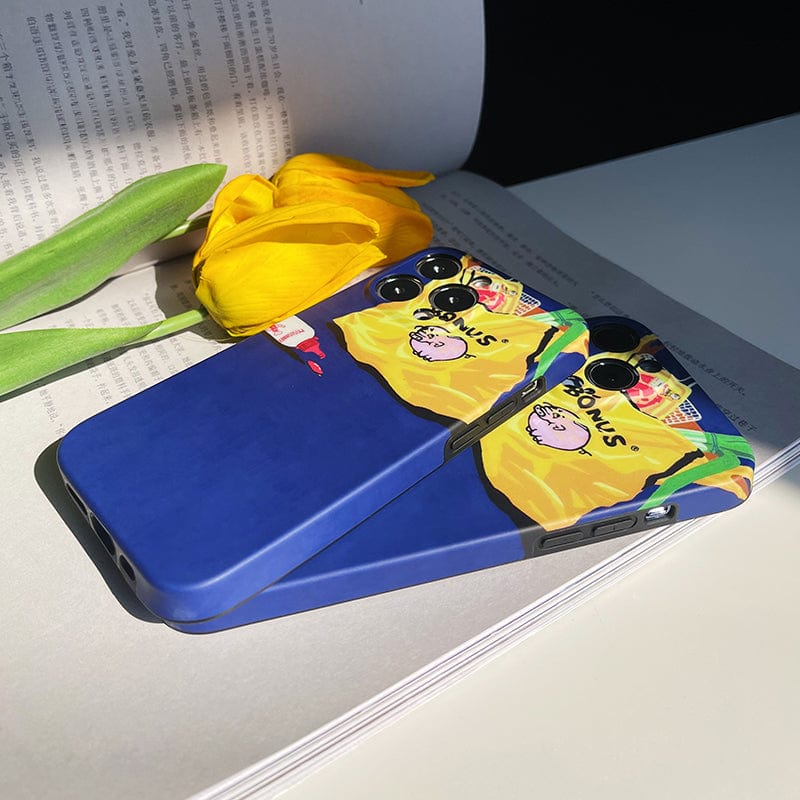 Two smartphones with vibrant blue Quirky Grocery Bag iPhone 16 Pro Max cases, showcasing a playful design of a person in a yellow construction outfit and hard hat, placed on an open book with a yellow tulip resting nearby.