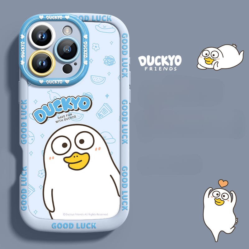 Smartphone with a blue "iPhone 16 Pro Max Yellow Duck Cartoon Case" featuring a cute yellow duck illustration and various texts such as "GOOD LUCK" and "HAVE FUN WITH DUCKYO." The background includes additional duck illustrations, all within shockproof, soft liquid silicone protection.