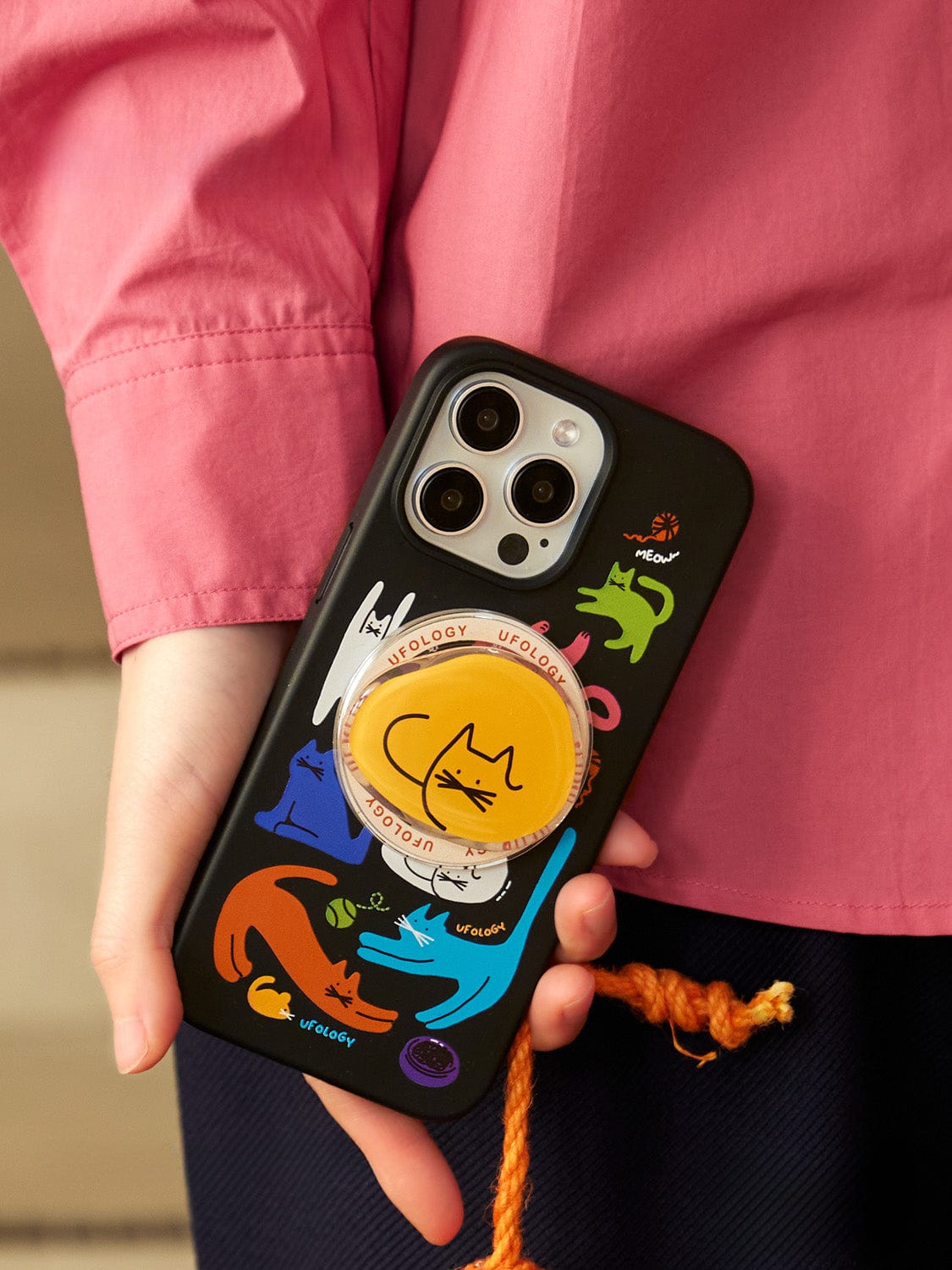 A person wearing a pink shirt and holding an iPhone 16 Pro Max with the Colorful Cats MagSafe iPhone 16 Pro Max Case, featuring a vibrant cat-themed design and an included cat-illustrated stand.